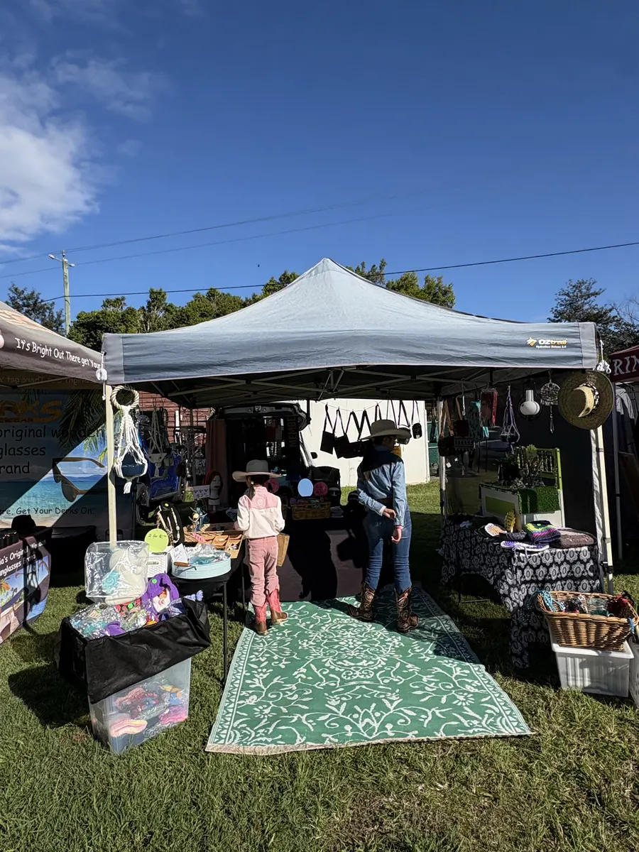 A market stall dressed with a rug, tables and goods, the stallholders standing under the marquee