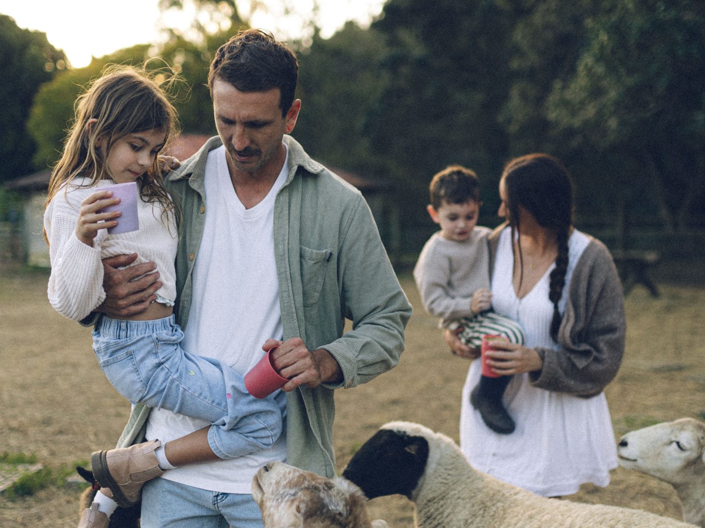 A family in the paddock at Historic Rivermill holding feed cups while the sheep and goats gather round