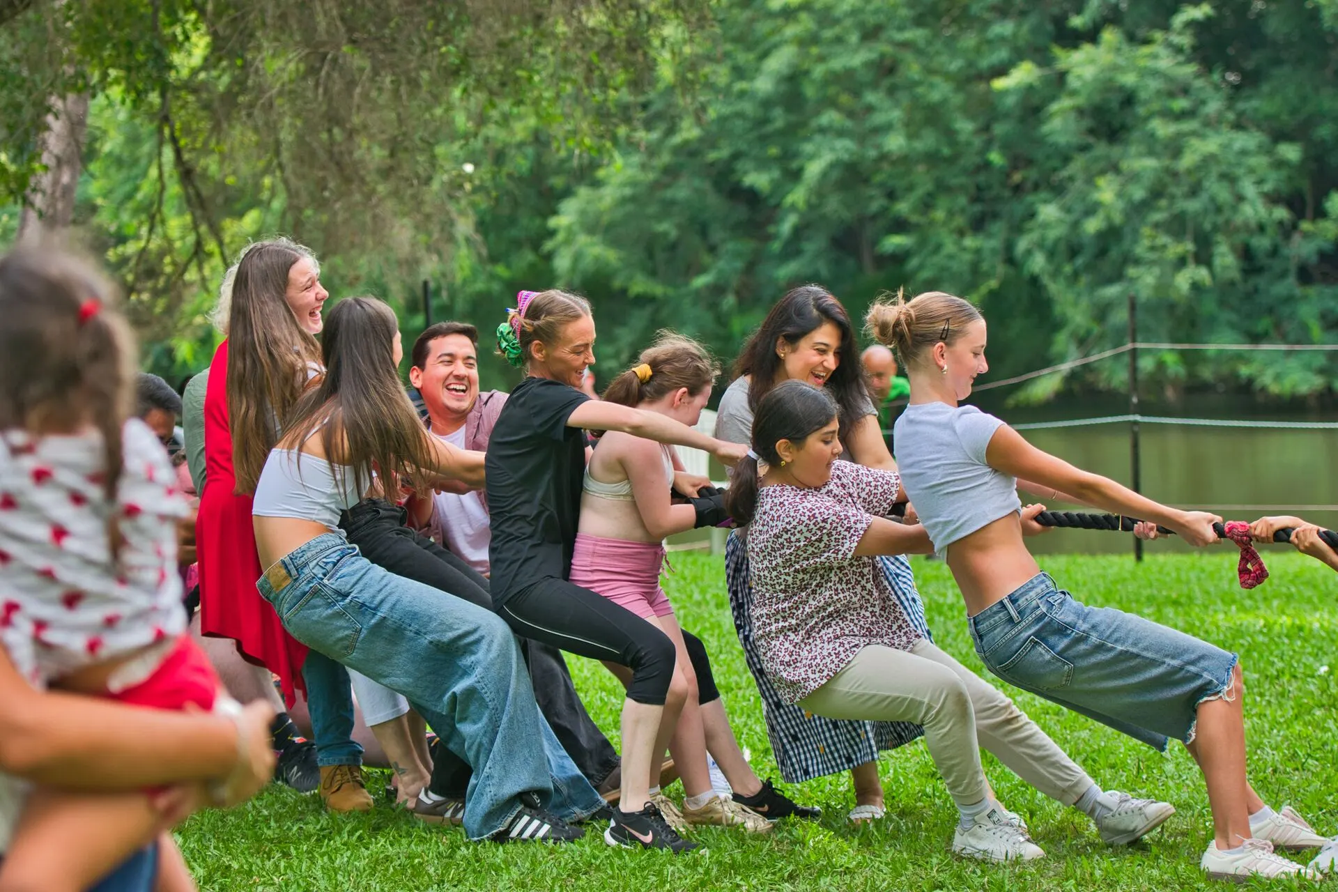 A laughing group playing tug of war on the riverside lawn at Historic Rivermill