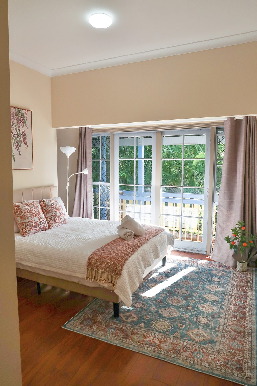 A queen bedroom at Rivermill Farm Stay with balcony doors opening onto palms