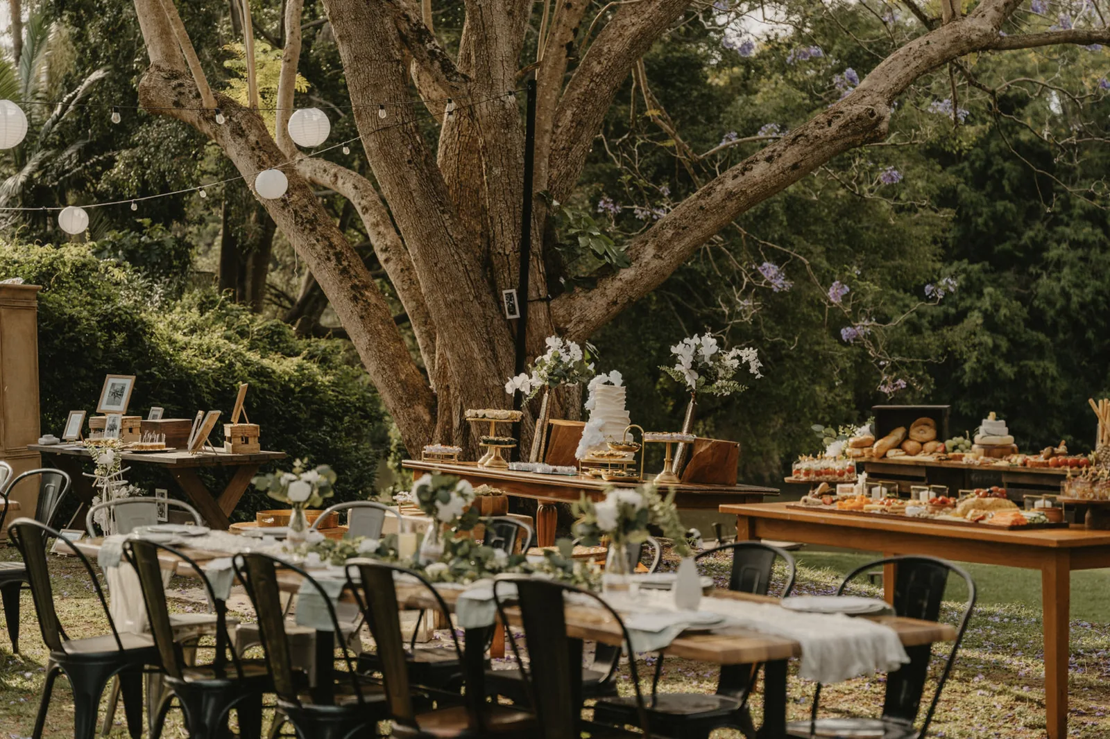 The bridal party seated at the long table with the Rivermill shed behind