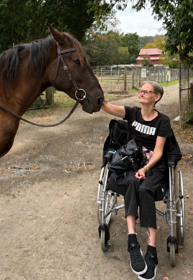 A smiling visitor in a wheelchair meeting one of the horses on the farm path at Historic Rivermill