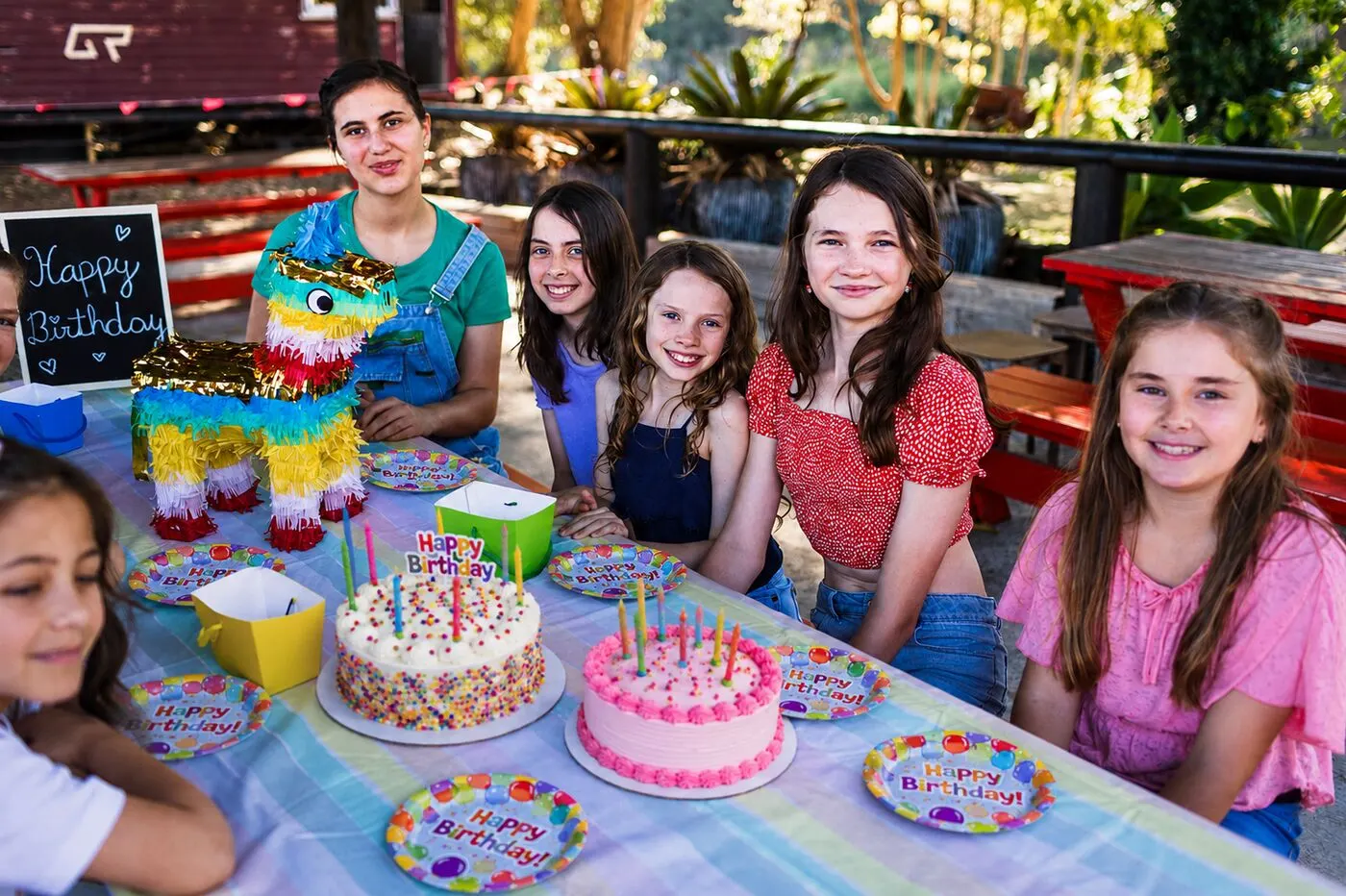 Kids' birthday party at the red tables, with cakes, plates and a piñata