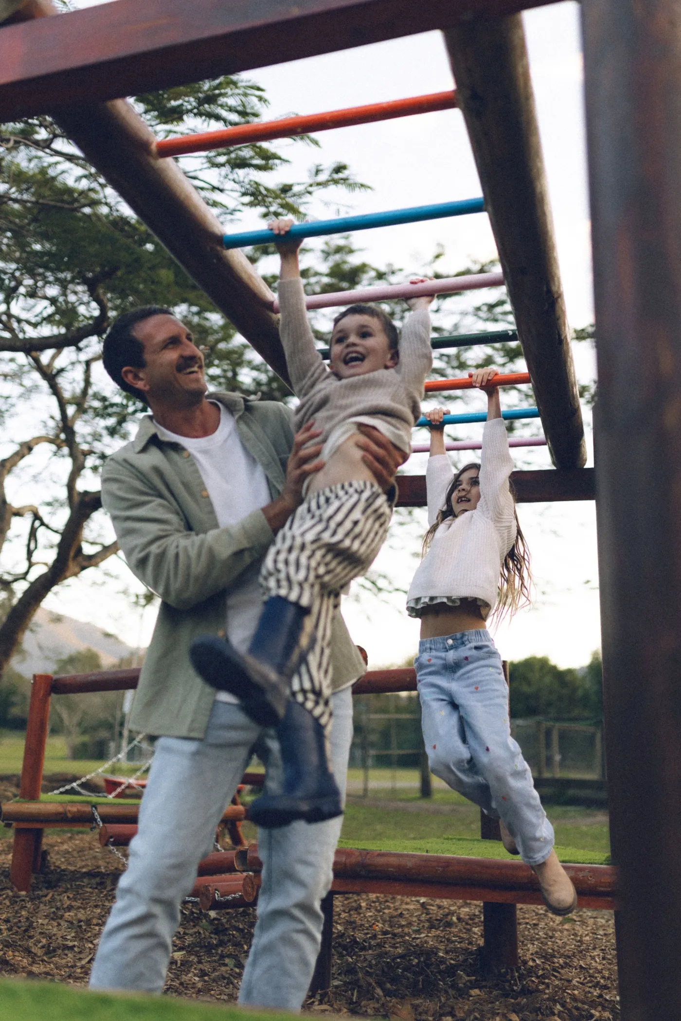 A dad helping his kids across the monkey bars at the Rivermill playground