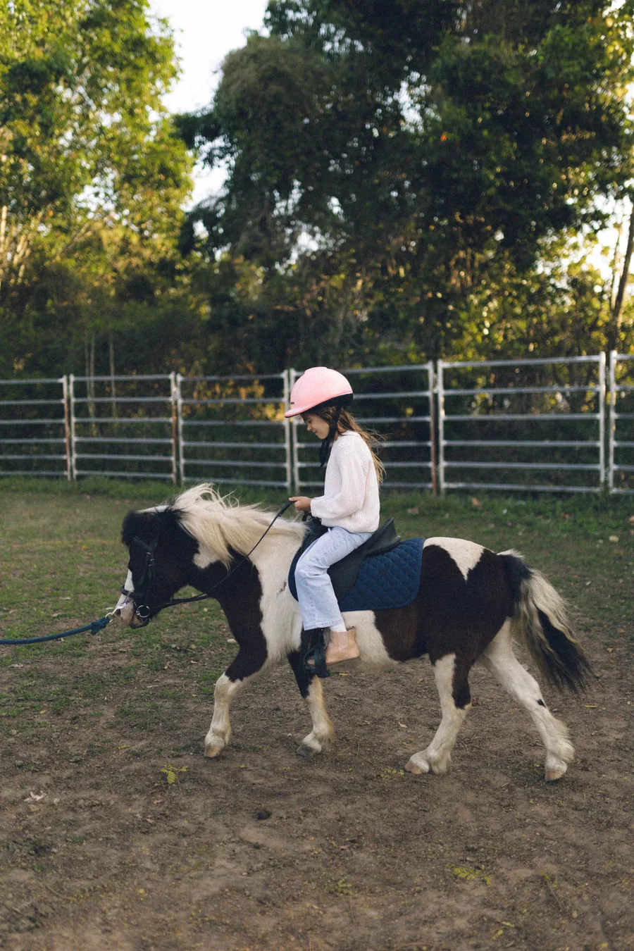 A young rider in a pink helmet aboard our gentle pinto pony, led by a handler
