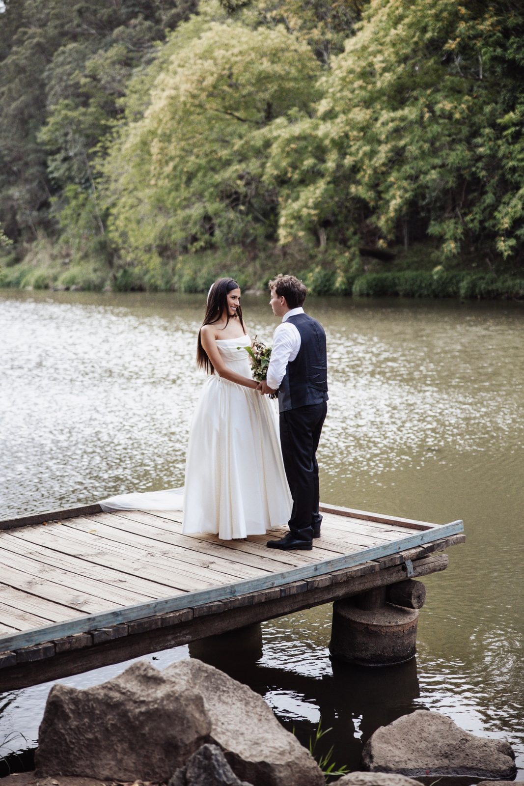 A bride and groom holding hands on the timber jetty over the Coomera River